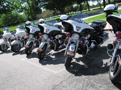 1991 Ford LTD Crown Victoria - row of black-and-white police motorcycles marked Police with red beacons and helmets parked angled on a paved lot.