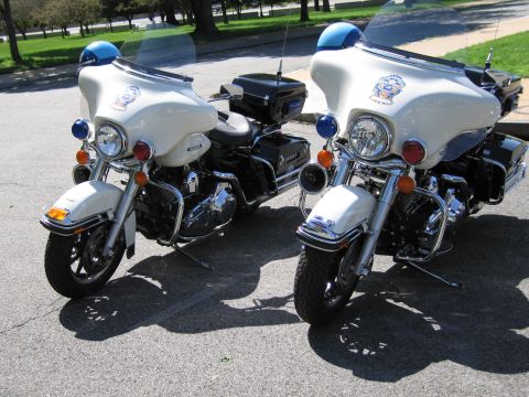 1991 Ford LTD Crown Victoria - Two white police motorcycles with blue roof beacons and fairing emblems parked next to each other on pavement.