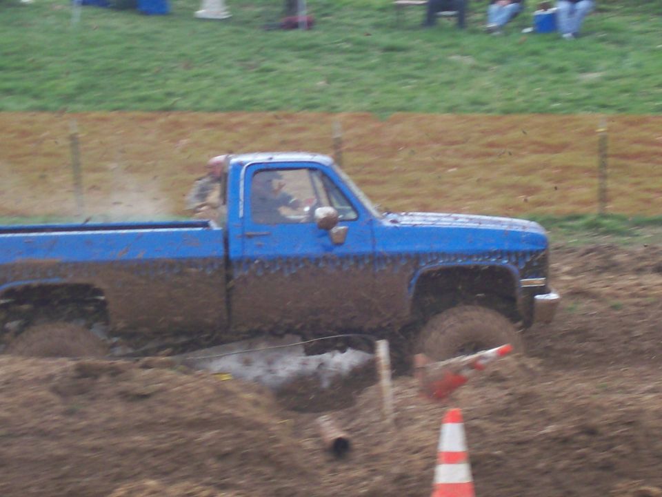 Side view of blue pickup truck driving through mud