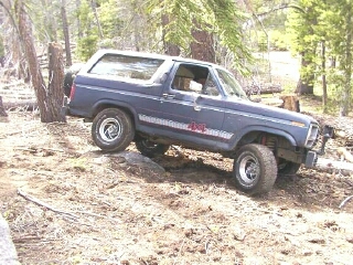 1986 Ford Bronco - Blue Ford Bronco navigates rough terrain, showing its off-road capabilities.