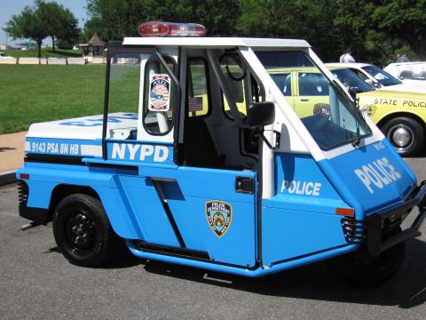 1991 Ford LTD Crown Victoria - blue-and-white NYPD three-wheeled police utility scooter with a red roof beacon parked on pavement.