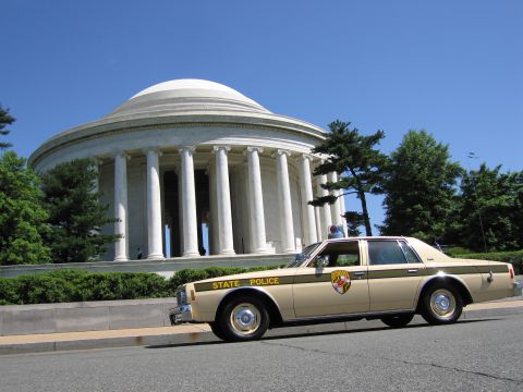 1991 Ford LTD Crown Victoria - tan and brown State Police sedan with a roof lightbar parked along the curb in front of the Jefferson Memorial under a clear blue sky.
