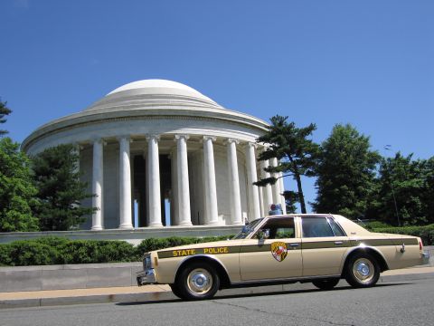 1991 Ford LTD Crown Victoria - tan State Police sedan sits at the curb in front of the columned Jefferson Memorial rotunda on a sunny day.