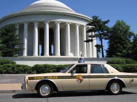 1991 Ford LTD Crown Victoria - tan State Police sedan with a colorful shield emblem on the door and a roof lightbar parked before the Jefferson Memorial columns.