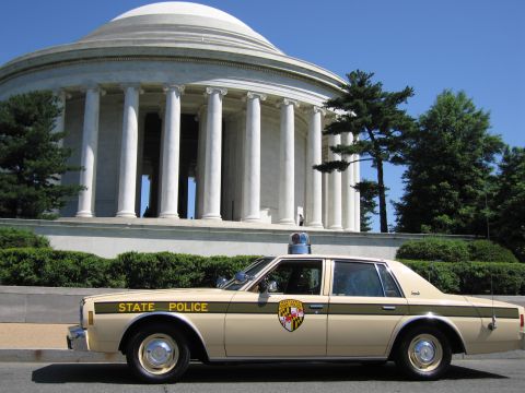 1991 Ford LTD Crown Victoria - Side profile of a tan State Police sedan with door shield emblem and roof beacon parked in front of the domed Jefferson Memorial.
