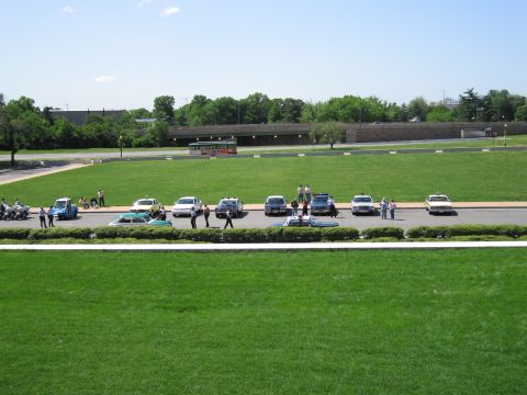 1991 Ford LTD Crown Victoria - distant view of several classic police cars lined up along a road in a large grassy park with people and motorcycles nearby.