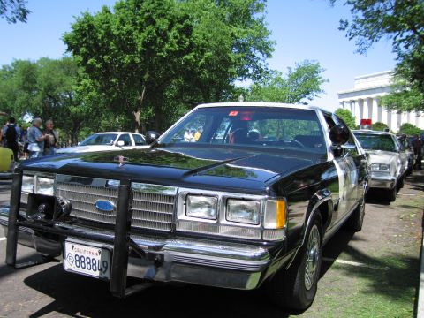 1991 Ford LTD Crown Victoria - black Ford four-door sedan fitted with a front push bar and California license plate parked near the Lincoln Memorial among other cars.