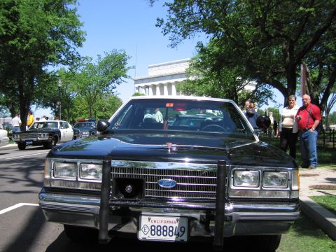 1991 Ford LTD Crown Victoria - Head-on view of a black Ford sedan with chrome grille and front push bar, the Lincoln Memorial visible through trees behind it.