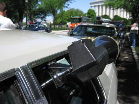 1991 Ford LTD Crown Victoria - Close-up of a black pillar-mounted spotlight on a white car, with other parked cars and the Lincoln Memorial in the background.