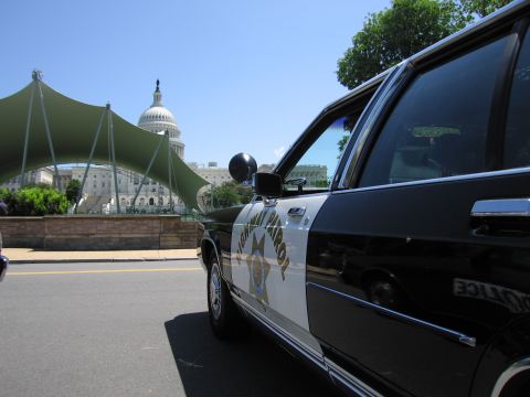 1991 Ford LTD Crown Victoria - black-and-white Highway Patrol sedan with star emblem and roof lights parked near a tent canopy with the U.S. Capitol dome behind.