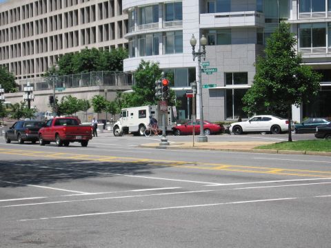 1991 Ford LTD Crown Victoria - red pickup, a dark SUV and a white Loomis armored truck wait at a downtown intersection of modern office buildings.