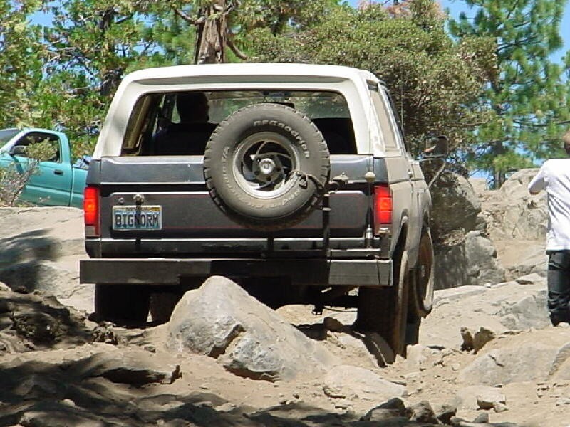 Rear view of dark blue Bronco with white top and BFGoodrich spare tire crawling over rocks, plate reads BIGNORM