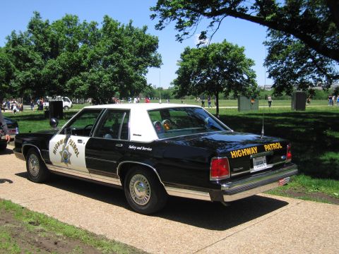 1991 Ford LTD Crown Victoria - rear three-quarter view of a black-and-white Highway Patrol sedan with star emblem parked on a paved park path.