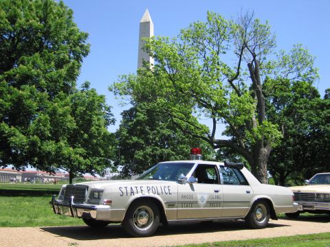 1991 Ford LTD Crown Victoria - tan Rhode Island State Police sedan parked on a park path with the Washington Monument rising through trees behind.