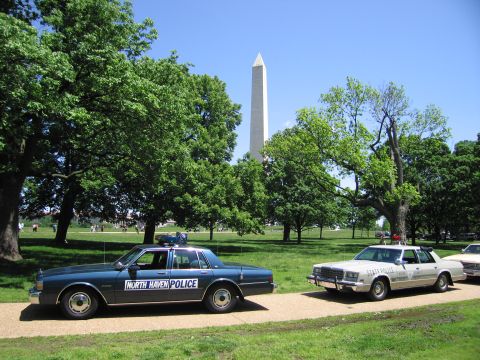 1991 Ford LTD Crown Victoria - blue North Haven Police sedan and a tan State Police cruiser parked on a park path beneath the Washington Monument.