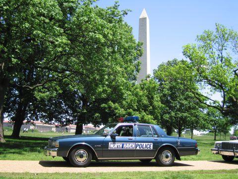 1991 Ford LTD Crown Victoria - dark blue "North Haven Police" sedan sits on a gravel path with the Washington Monument and trees behind it.
