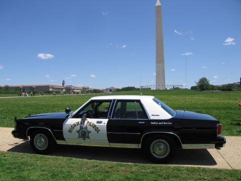 1991 Ford LTD Crown Victoria - black-and-white Highway Patrol sedan with a star door shield parked on grass beneath the Washington Monument.