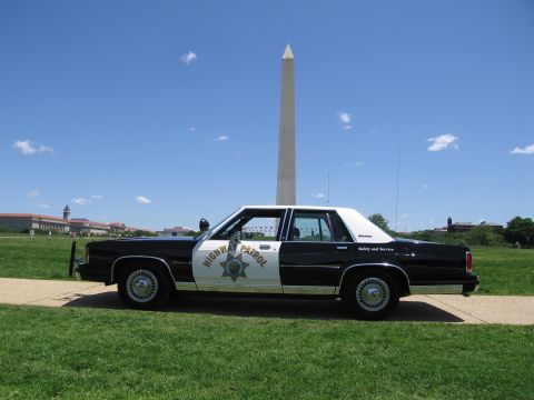 1991 Ford LTD Crown Victoria - black-and-white Highway Patrol sedan with a gold star shield sits on grass below the Washington Monument and blue sky.