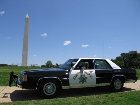 1991 Ford LTD Crown Victoria - black-and-white Highway Patrol sedan fitted with a front push bar, parked on grass before the Washington Monument.