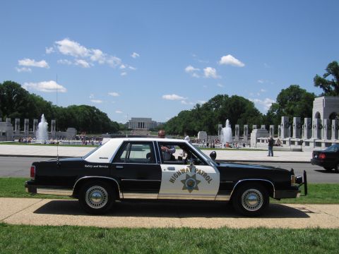 1991 Ford LTD Crown Victoria - black-and-white Highway Patrol sedan parked along a road with the WWII Memorial fountains and Lincoln Memorial behind.