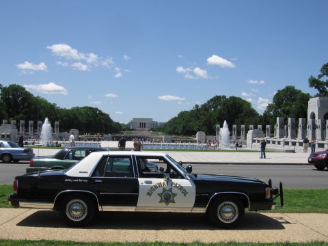 1991 Ford LTD Crown Victoria - black-and-white Highway Patrol sedan parked on grass with the WWII Memorial fountains and Lincoln Memorial in the distance.