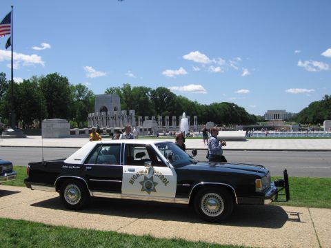 1991 Ford LTD Crown Victoria - black-and-white Highway Patrol sedan parked near the WWII Memorial fountains with several people standing around it.
