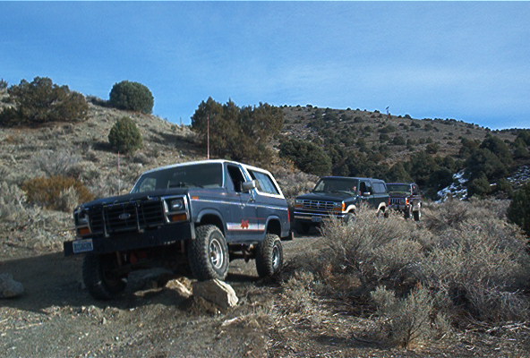 Dark blue lifted Ford Bronco on a desert hillside with two 4x4s behind