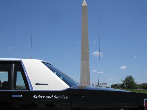 1991 Ford LTD Crown Victoria - Rear quarter of a black-and-white Crown Victoria police car with "Safety and Service" lettering below the Washington Monument.