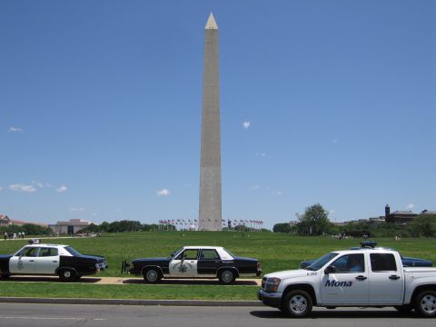 1991 Ford LTD Crown Victoria - Black-and-white police sedans and a white "Mona" pickup truck parked along a road beneath the Washington Monument.