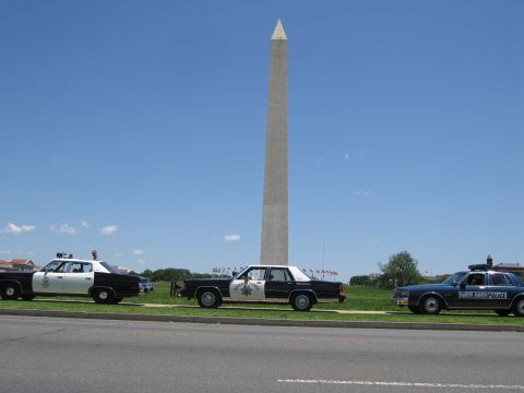 1991 Ford LTD Crown Victoria - Three police sedans, including black-and-white and dark blue cars, parked on grass around the Washington Monument.