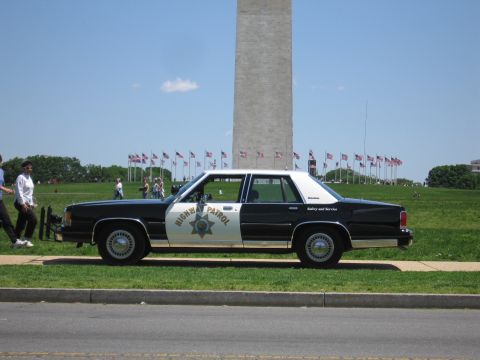 1991 Ford LTD Crown Victoria - black-and-white police sedan marked Highway Patrol sits curbside in front of the Washington Monument under a clear sky.
