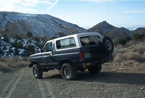 1986 Ford Bronco - This Ford Bronco is parked on a dirt road with snow-dusted mountains in the distance.