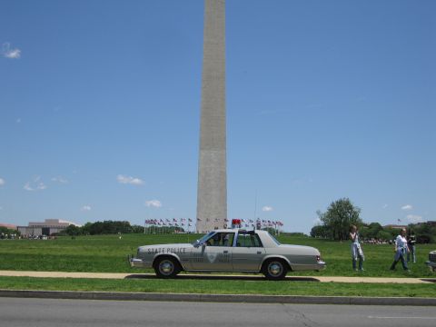1991 Ford LTD Crown Victoria - silver sedan marked State Police sits curbside on the grass in front of the Washington Monument under blue sky.