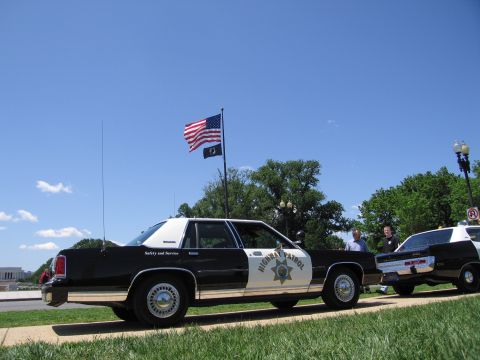 1991 Ford LTD Crown Victoria - rear quarter of a black-and-white Highway Patrol sedan is shown near a flagpole, with another patrol car alongside.