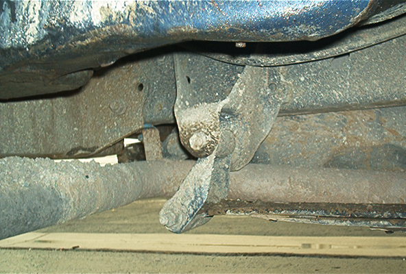 Underside view of a vehicle frame and crossmember with rusty steering linkage