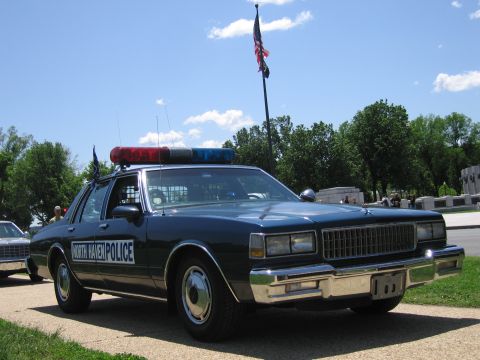 1991 Ford LTD Crown Victoria - dark blue North Haven Police sedan with a red-and-blue roof light bar is parked on a tree-lined path.