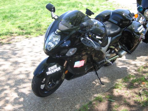 1991 Ford LTD Crown Victoria - black sportbike marked State Trooper with a small American flag decal stands on its kickstand on a paved path.