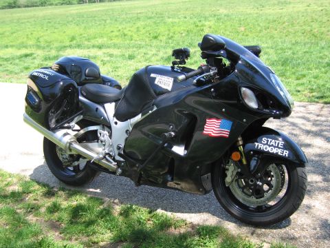 1991 Ford LTD Crown Victoria - black State Trooper sportbike with a US flag decal is shown from the right rear, parked on a paved path beside grass.