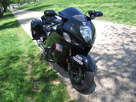 1991 Ford LTD Crown Victoria - black State Trooper sportbike with a US flag decal faces the camera, parked on a paved path lined with grass.