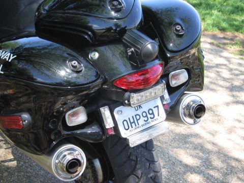 1991 Ford LTD Crown Victoria - Tail end of a black motorcycle showing a UK plate reading OHP997, dual chrome exhausts, and partial police lettering.