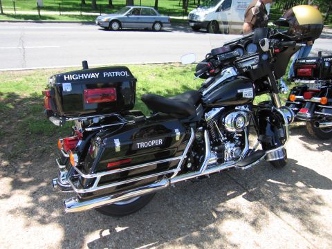 1991 Ford LTD Crown Victoria - black Harley-Davidson police touring bike lettered Highway Patrol and Trooper, parked roadside with others behind it.