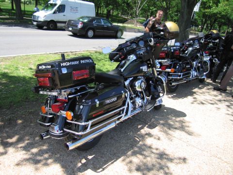 1991 Ford LTD Crown Victoria - Several black police touring motorcycles lettered Highway Patrol and Trooper lined up along a roadside, officer nearby.