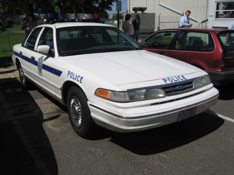 1991 Ford LTD Crown Victoria - white Ford Crown Victoria police sedan with blue Police lettering and shield, parked beside a red station wagon.