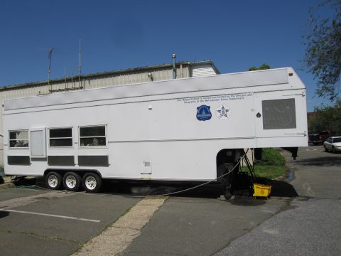 1991 Ford LTD Crown Victoria - long white triple-axle gooseneck trailer serving as a Metropolitan Police Department mobile kitchen parked in a lot.