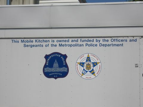 1991 Ford LTD Crown Victoria - Close-up of a white trailer panel reading the mobile kitchen is funded by officers, beside two Metropolitan Police seals.