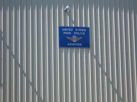 1991 Ford LTD Crown Victoria - blue United States Park Police Aviation sign with a winged badge mounted on a ribbed gray metal building wall.