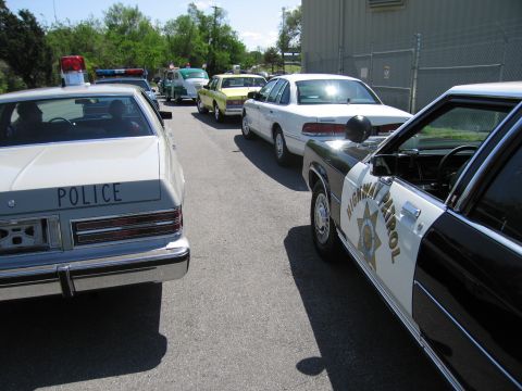1991 Ford LTD Crown Victoria - lineup of police cars on pavement including a Police-marked sedan and a black-and-white Highway Patrol Crown Victoria.
