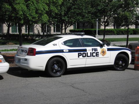 1991 Ford LTD Crown Victoria - white Dodge Charger police sedan lettered FBI Police with badge and unit 124, parked under trees along a street.