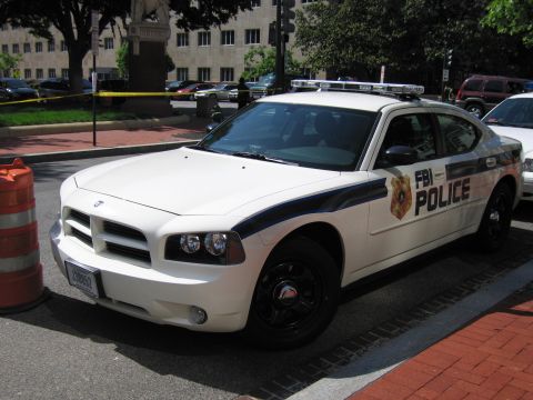 1991 Ford LTD Crown Victoria - white Dodge Charger sedan marked FBI POLICE sits at a taped-off curb in front of a stone government building.