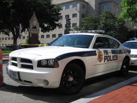 1991 Ford LTD Crown Victoria - white Dodge Charger FBI POLICE cruiser viewed from the front, parked near a statue and a large stone building.